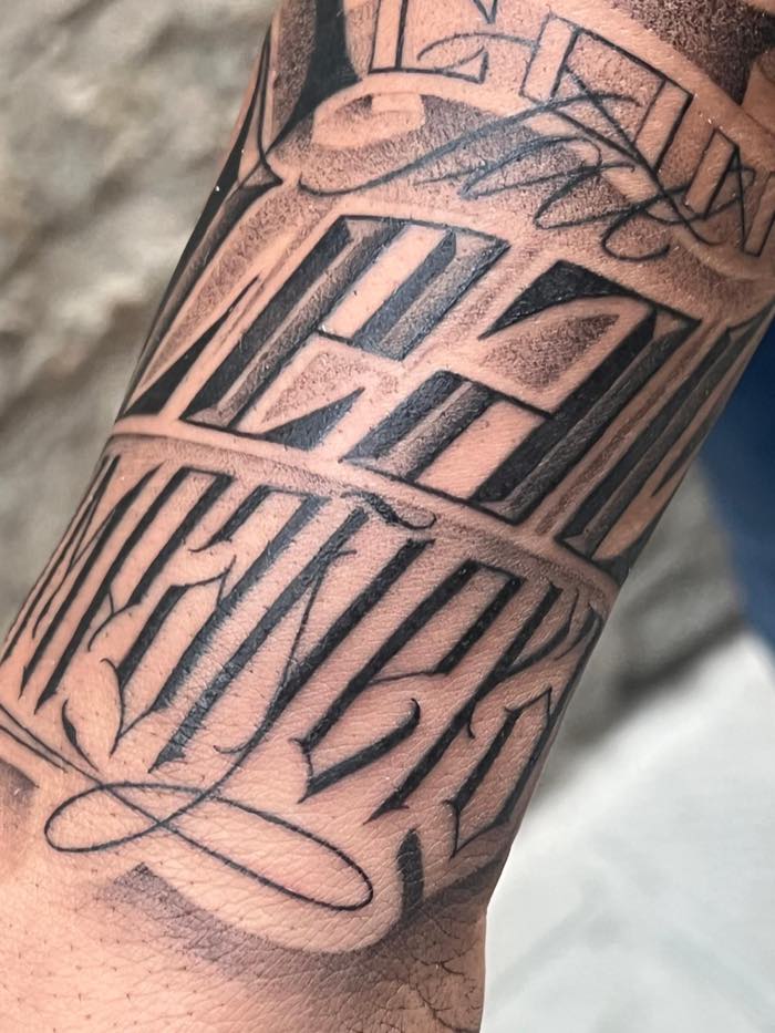 Lettering blackletter con ombreggiature grigie e svolazzi calligrafici, su avambraccio guarito