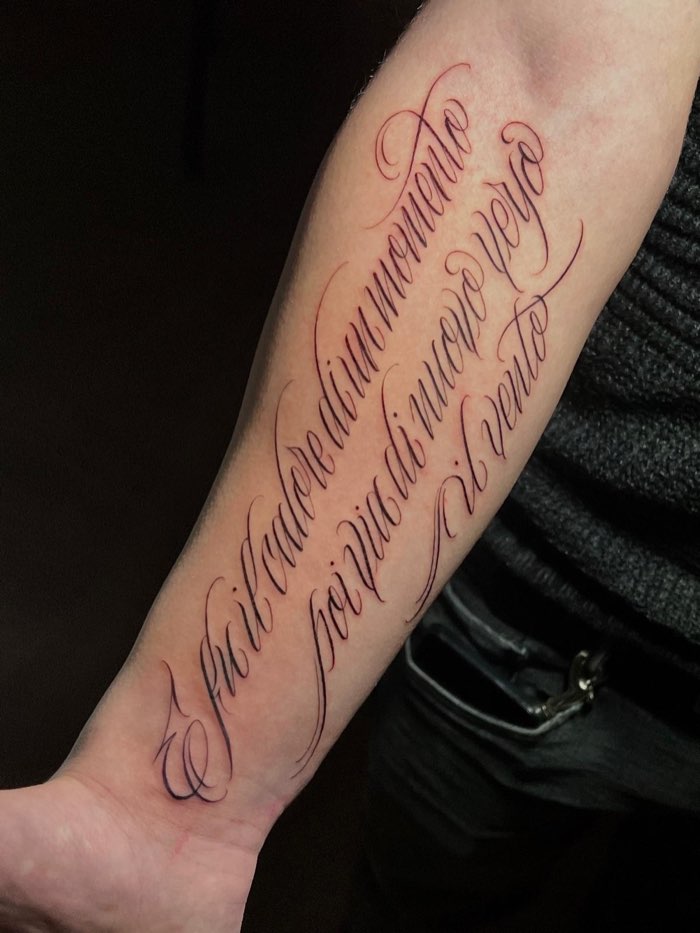 Frase in corsivo calligrafico fine line lungo l’avambraccio, linee sottilissime